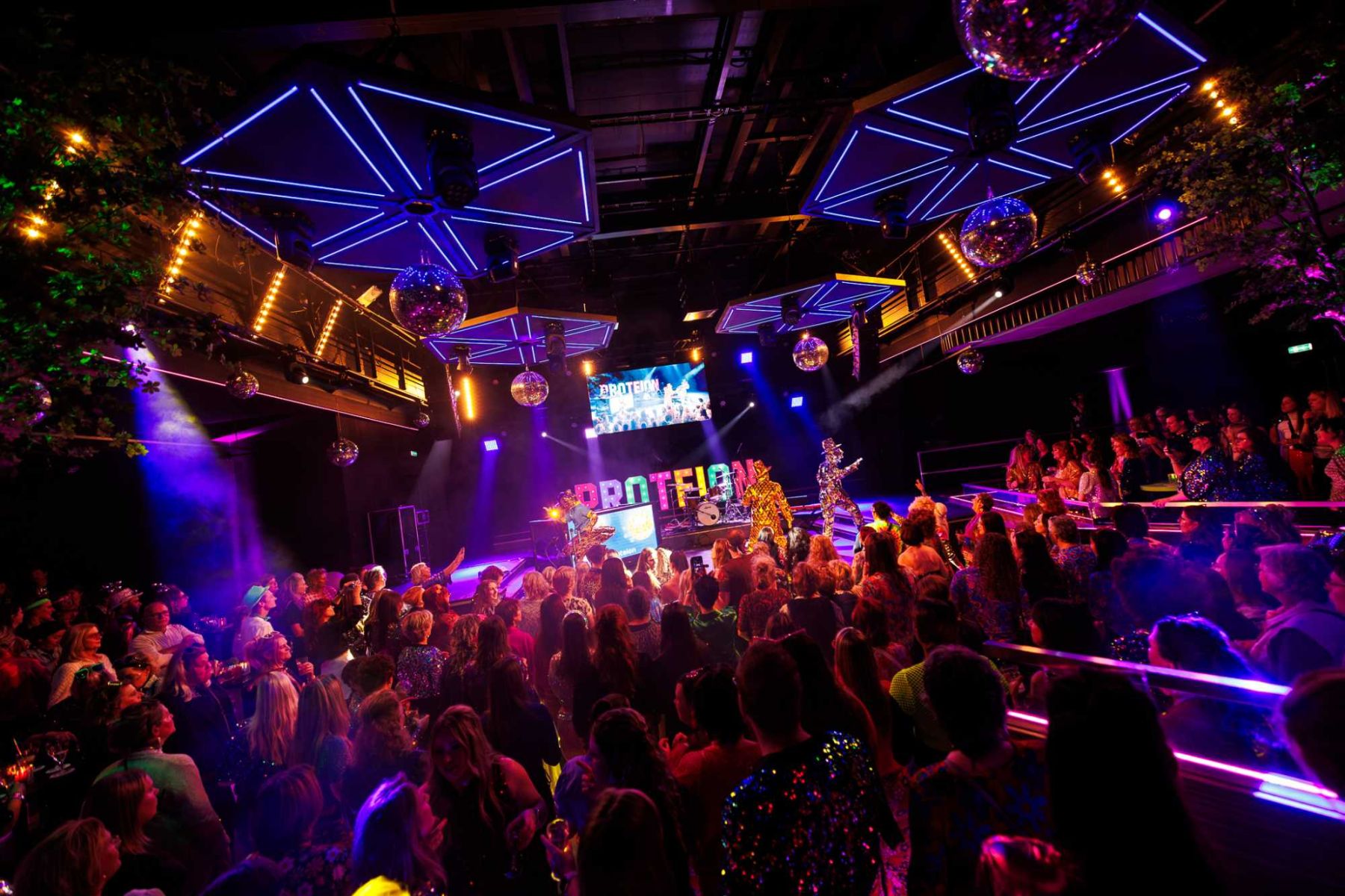 Sfeervol personeelsfeest in discothema met een volle dansvloer, kleurrijke verlichting, discoballen en live entertainment.